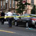 Crowd Ambushed — SUV Sprays Bullets Police and crime scene tape on city street.