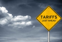 Tariff Bomb Over Smoke Yellow sign saying tariffs just ahead cloudy sky