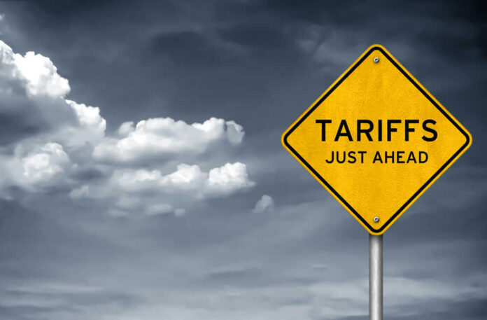 shutterstock_1037228893 Yellow sign saying tariffs just ahead cloudy sky
