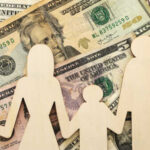 Default Tsunami Slams Millions Wooden figures representing a family on a background of US dollar bills