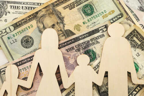 Business,Concept,Of,Family,Economy,And,Expenses.,Dollar,Bills,And Wooden figures representing a family on a background of US dollar bills
