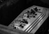 Coffin with flowers inside a dark burial plot.