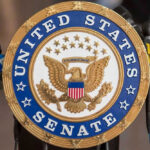United States Senate seal with microphones in front.