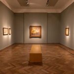 Interior of an art gallery with paintings on the walls and a wooden bench in the center