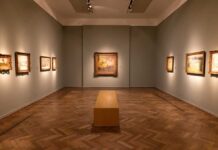 Interior of an art gallery with paintings on the walls and a wooden bench in the center