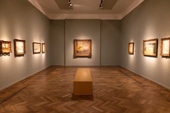 Interior of an art gallery with paintings on the walls and a wooden bench in the center