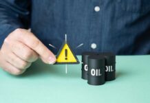 Big Oil Probe: Floodlights On A person holding a warning sign next to oil barrels