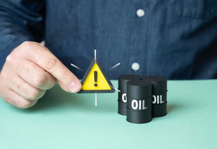 Man,Warns,About,Oil,Supplies.,Fear,Of,Rising,Prices,,Falling A person holding a warning sign next to oil barrels