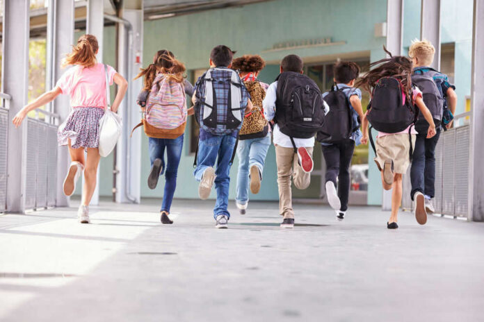 shutterstock_388660693 Children running with backpacks outside a school building.