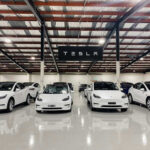 White Tesla cars displayed in showroom with Tesla sign.