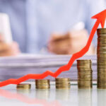 Profit Shock Rockets Wall Street Stacked coins with upward red arrow graph in foreground.