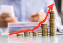 Profit Shock Rockets Wall Street Stacked coins with upward red arrow graph in foreground.