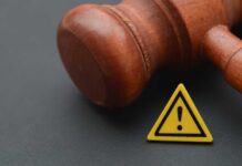 Judge Slams Brakes On Extradition Clash Wooden gavel with a yellow warning triangle sign on dark surface