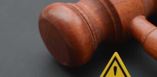 Wooden gavel with a yellow warning triangle sign on dark surface
