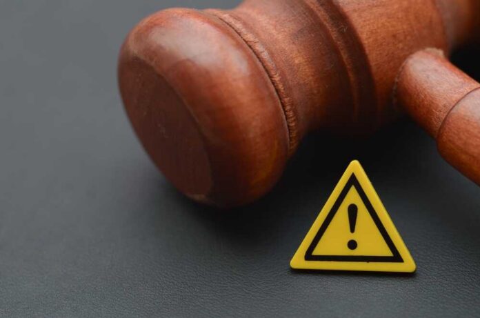 Judge's,Gavel,Is,Juxtaposed,With,A,Yellow,Caution,Sign,Featuring Wooden gavel with a yellow warning triangle sign on dark surface