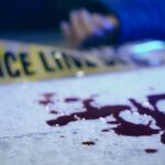 Blood on pavement with police tape and a hand in the background