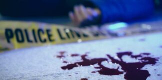 Blood on pavement with police tape and a hand in the background