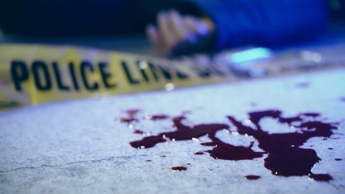 Blood on pavement with police tape and a hand in the background