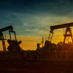 Oil pumpjacks silhouetted at sunset on a rural field