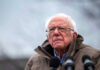 Bernie’s Cash Bomb Hits Elderly man in glasses speaks at an outdoor event.