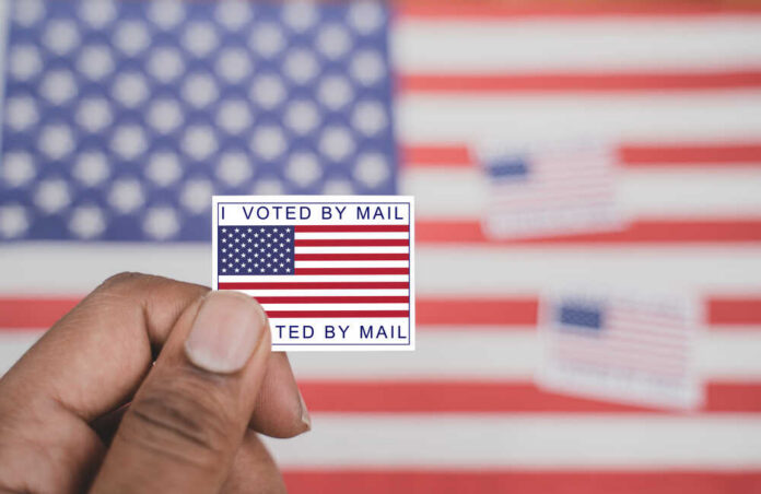 Holding,I,Voted,My,Mail,Sticker,In,Hands,With,Us Hand holding a vote-by-mail sticker with U.S. flag