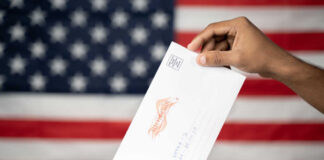 Hand inserting mail-in ballot envelope into ballot box