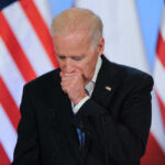 Joe Biden stands at a podium with U.S. flags in the background