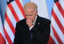 Joe Biden stands at a podium with U.S. flags in the background