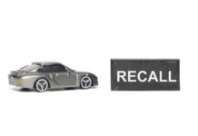 Blackout Recall Slams U.S. Automaker A miniature gray sports car next to a black sign that reads 'RECALL'