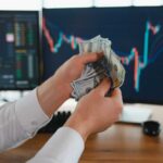 Wall Street Fast Lane to Trump? Person holding cash in front of stock market charts on computer screens