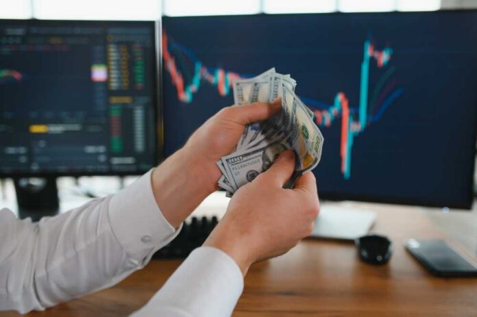 Holding,Dollar,Bills,In,The,Stock,Market.,Investors,Counting,Money Person holding cash in front of stock market charts on computer screens