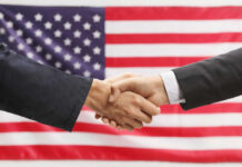 Huge Power Shift In American Business Two hands shaking in front of American flag