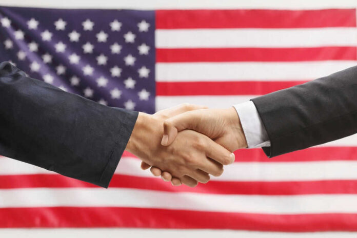 shutterstock_2454737145 Two hands shaking in front of American flag