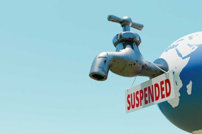 Faucet on a globe with a suspended sign against a clear sky