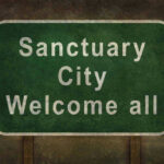 Green sign reading Sanctuary City Welcome all