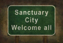 Green sign reading Sanctuary City Welcome all