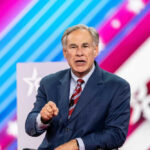Texas Bombshell: Abbott Suddenly On The Ropes Greg Abbott speaking on stage in a blue suit and red striped tie