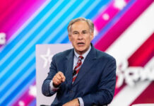 Greg Abbott speaking on stage in a blue suit and red striped tie
