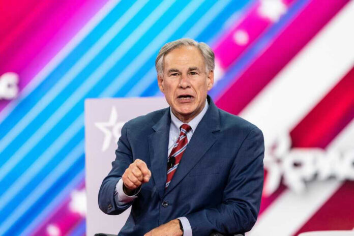 shutterstock_2188817463 Greg Abbott speaking on stage in a blue suit and red striped tie