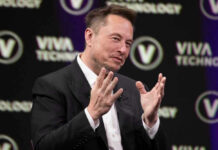Elon Musk speaking on stage with hands raised during a talk